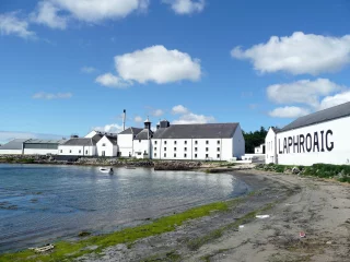 Distillerie Laphroaig au bord de la mer sur l’île d’Islay, avec ses bâtiments blancs emblématiques et le nom “LAPHROAIG” peint en grandes lettres noires.